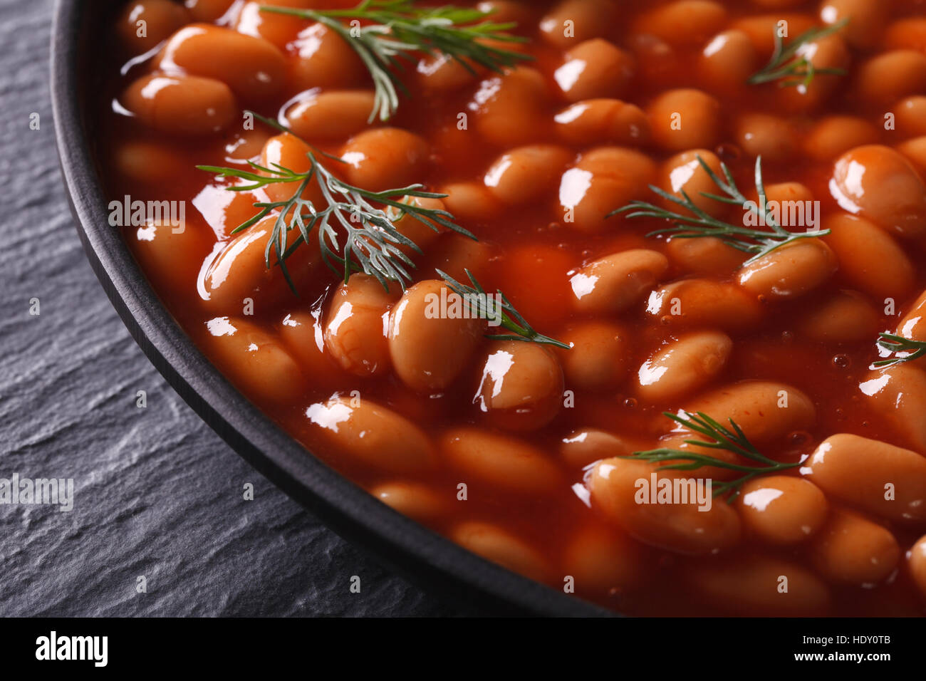 weiße Bohnen in Tomatensauce mit Dill in einem schwarzen Schale Nahaufnahme. horizontale Stockfoto