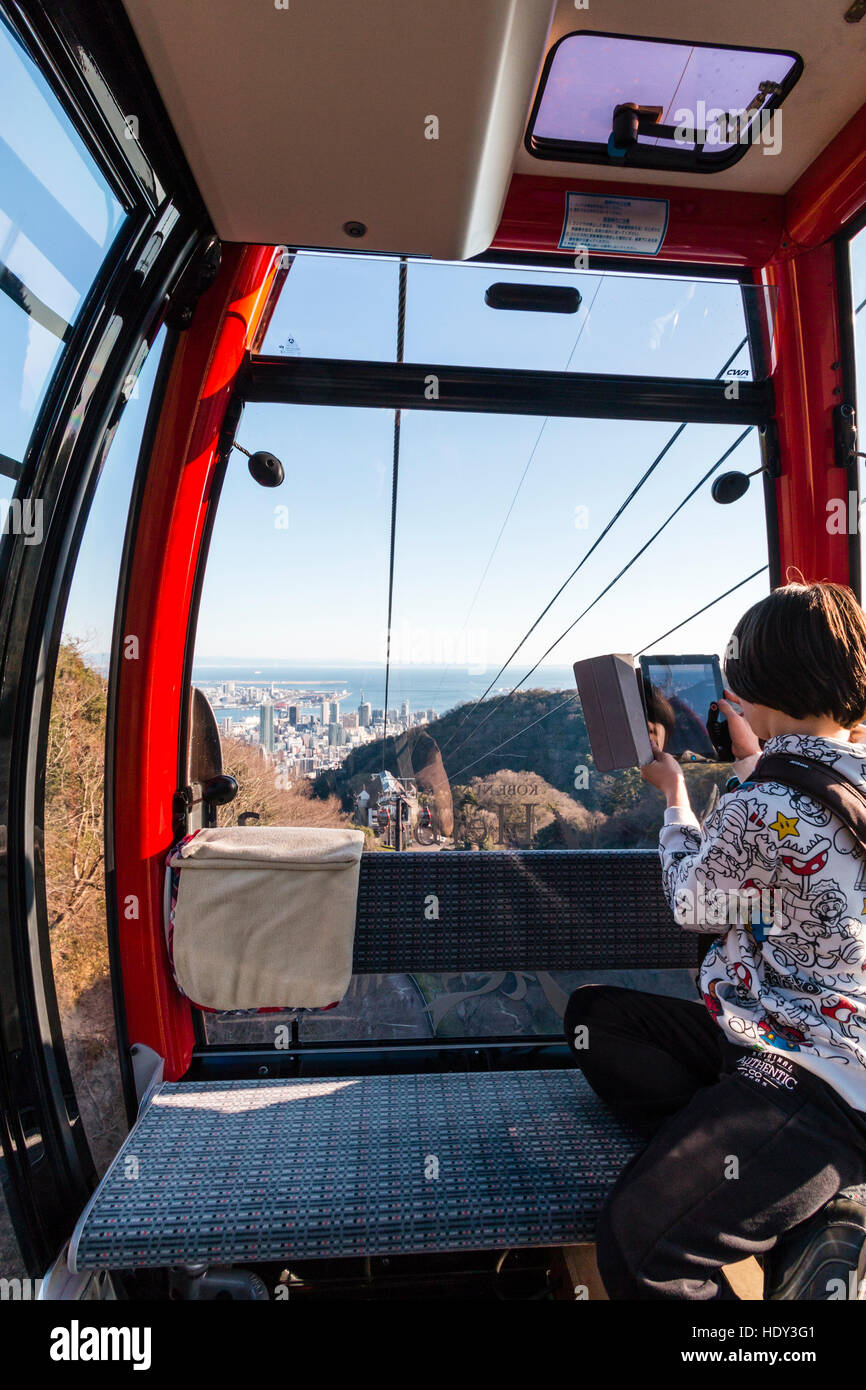 Japan, Kobe. Kaukasische junge männliche Jugendliche, 14-15 Jahre alt, in der Seilbahn auf Shin-Seilbahn, während der Fahrt Filmen mit einem I-pad, tablet. Stockfoto