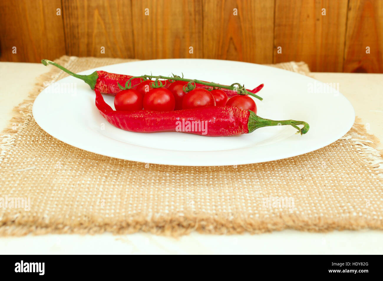 Zweig der rote Kirschtomaten und zwei Pods von Chilischoten auf dem Teller Stockfoto