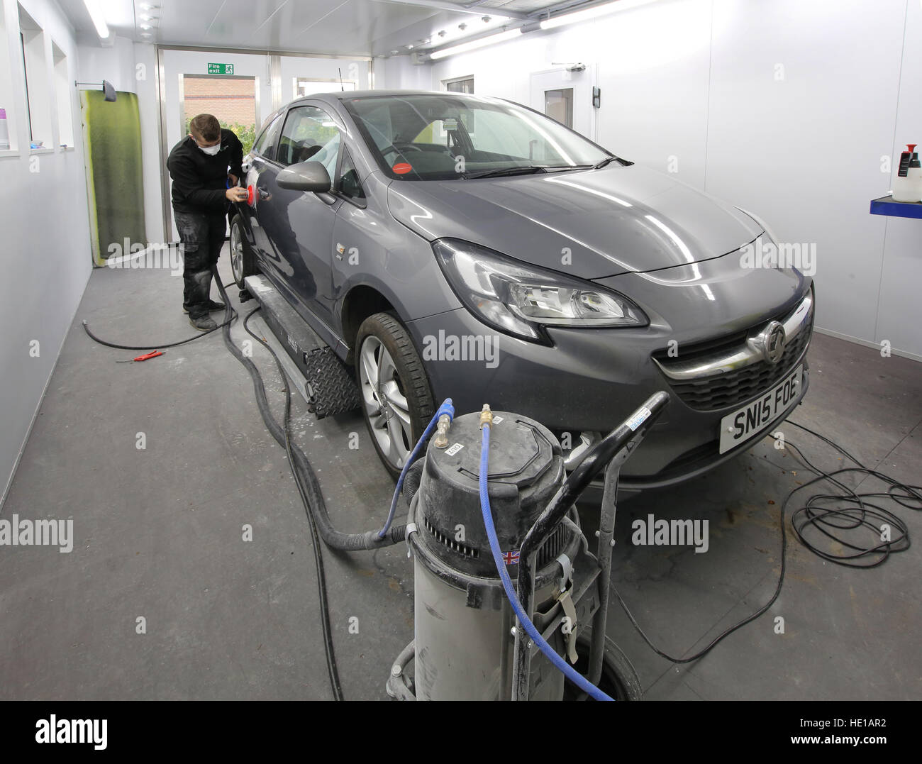 Ein Mechaniker nutzt eine elektrische Sandpapierschleifmaschine, um Spachtel auf eine reparierte Auto vor der Neulackierung zu reiben. Stockfoto