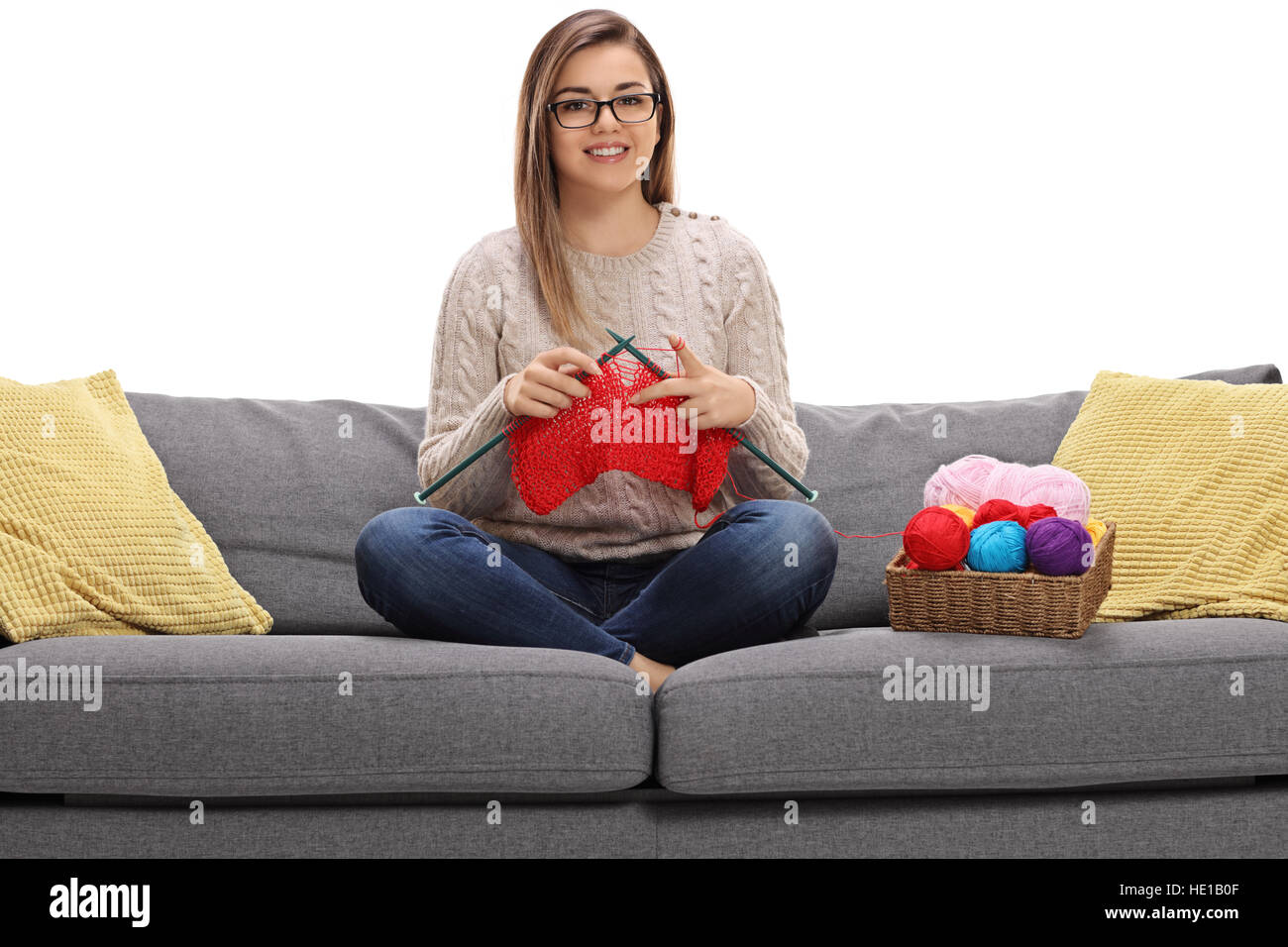 Fröhliche Mädchen auf einem Sofa stricken und schaut in die Kamera, die isoliert auf weißem Hintergrund Stockfoto