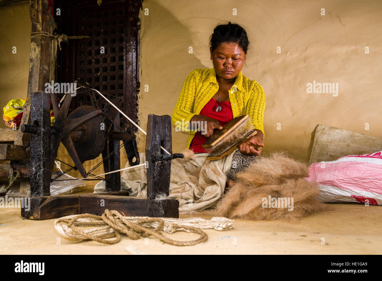 Eine lokale Frau dreht sich Schafwolle mit einem traditionellen Spinnrad vor einem Haus Stockfoto