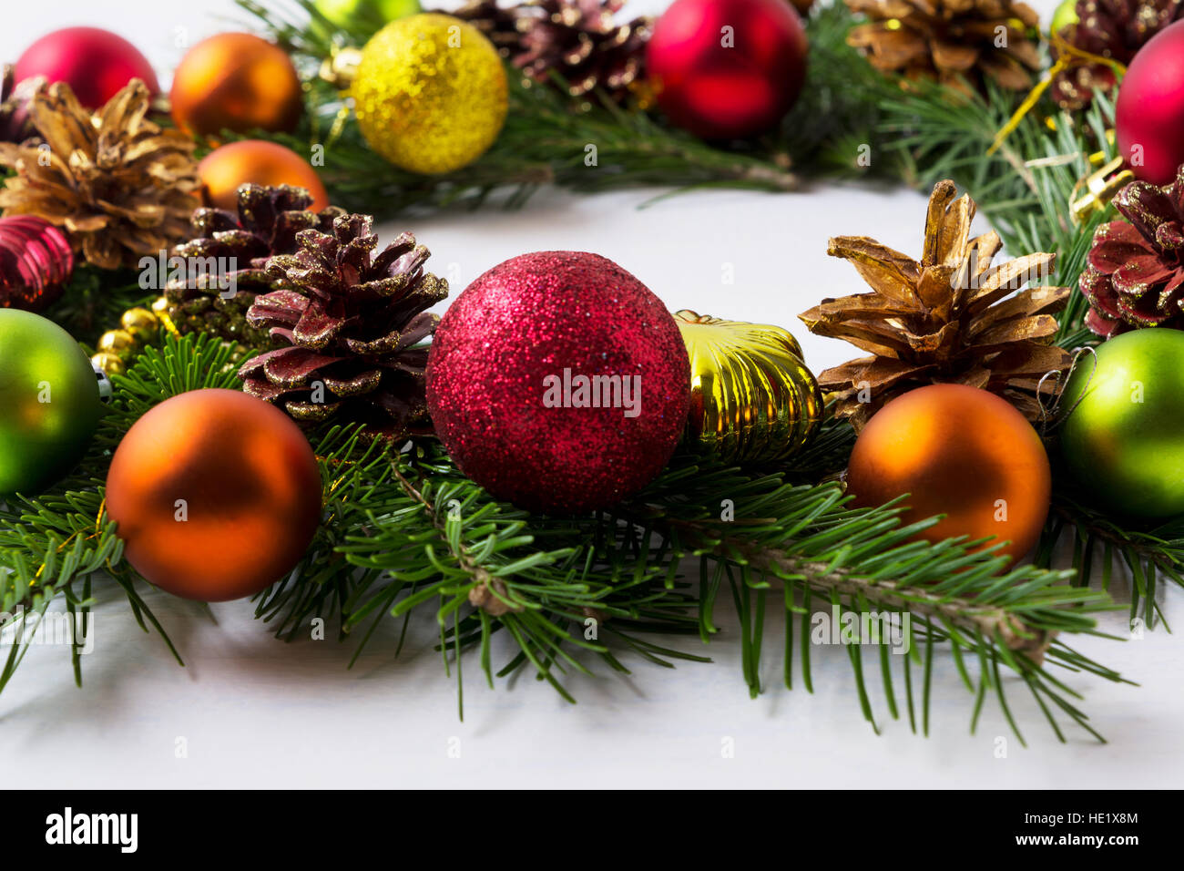 Adventskranz mit rot, grün, orange und gelben Ornamenten. Weihnachts-Dekoration mit bunten Glaskugeln und Tannenzapfen. Stockfoto