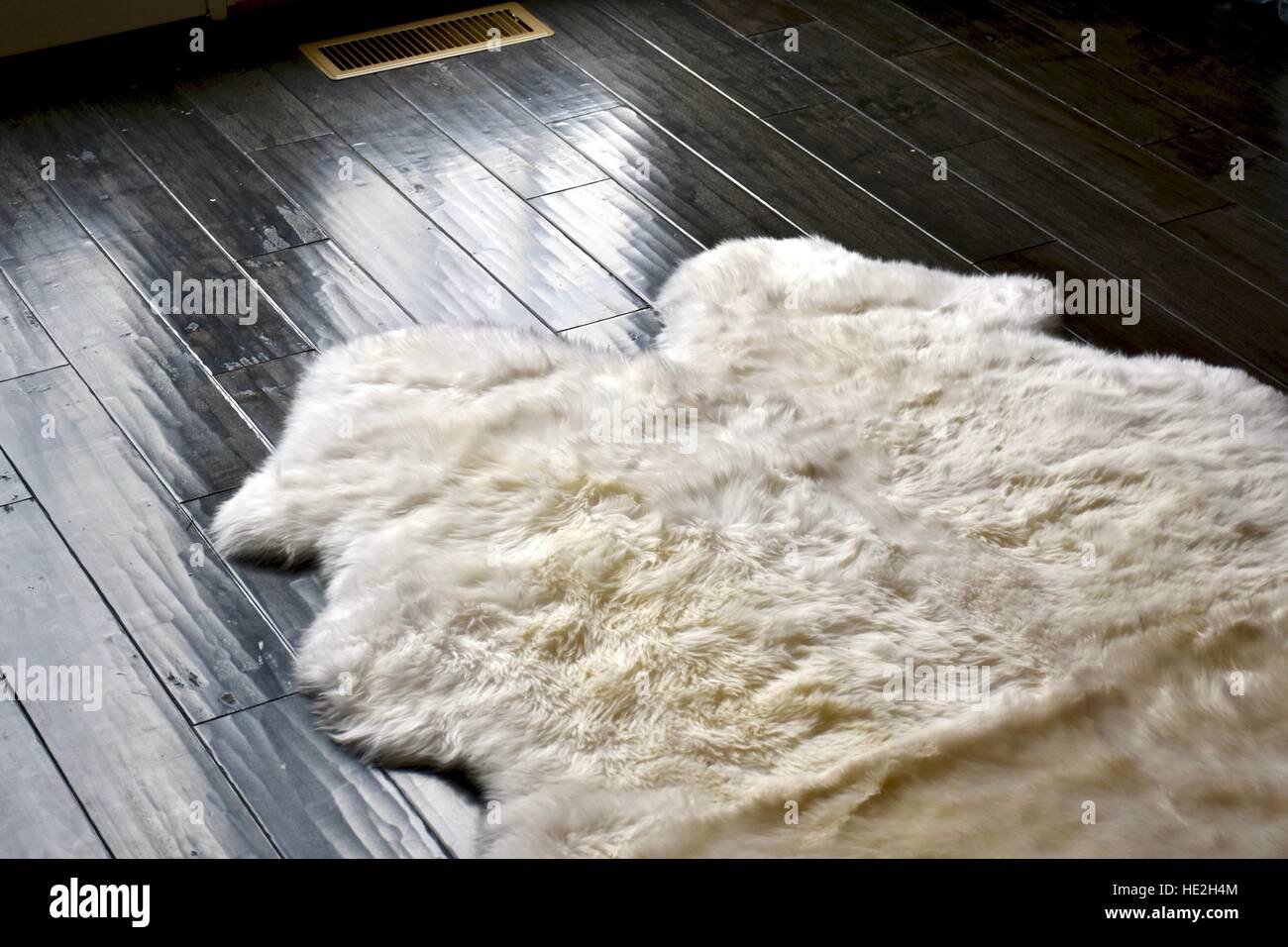 Ein weißes Schaf Haut Teppich auf einem dunklen Parkettboden Stockfoto