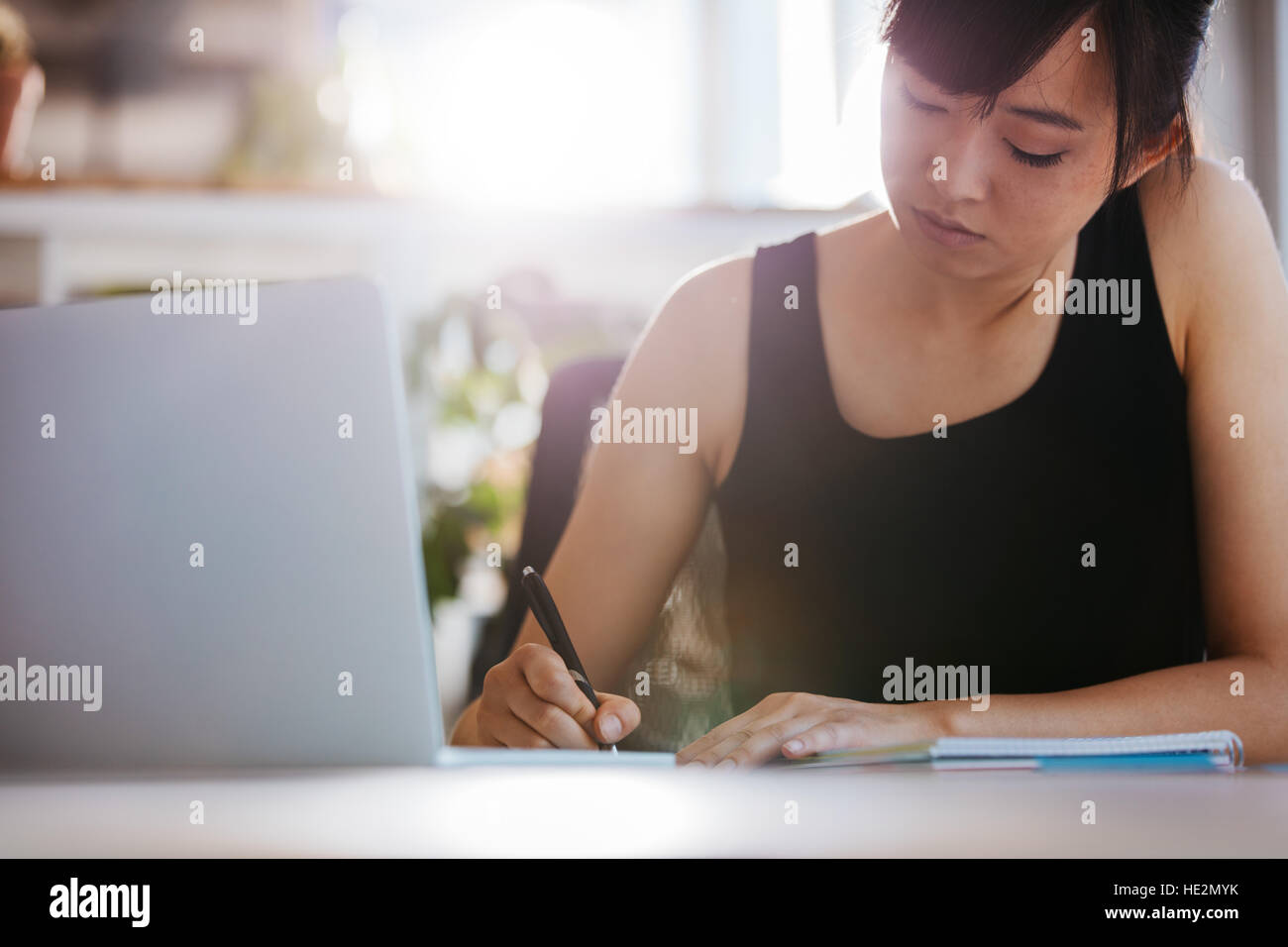 Junge Frau an ihrem Schreibtisch Notizen arbeiten. Asiatische Geschäftsfrau mit Laptop schreibt auf ein Dokument in ihrem Büro. Stockfoto