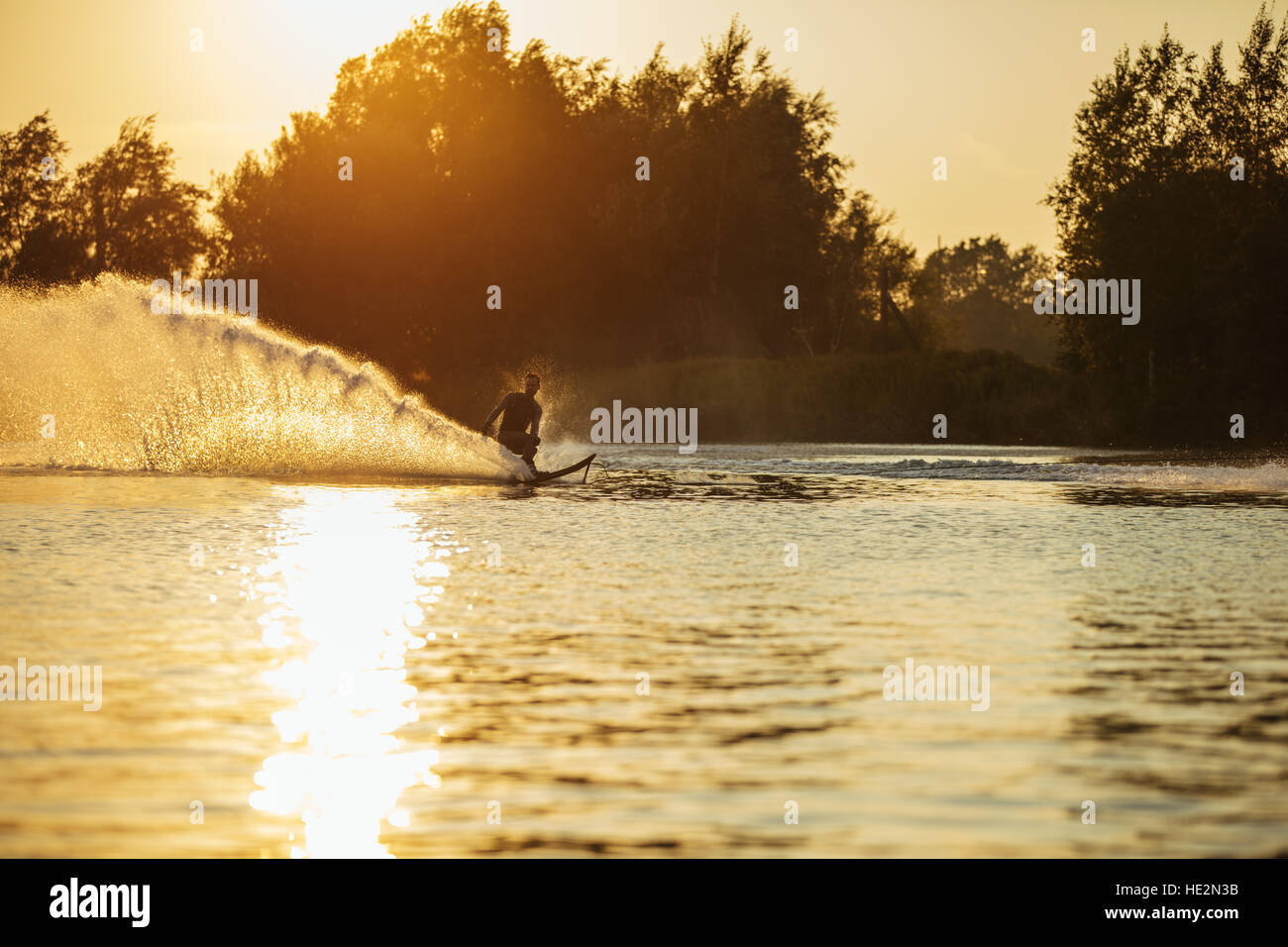 Mann-Wasserski auf See mit Spritzwasser. Mann Wakeboarden bei Sonnenuntergang. Stockfoto