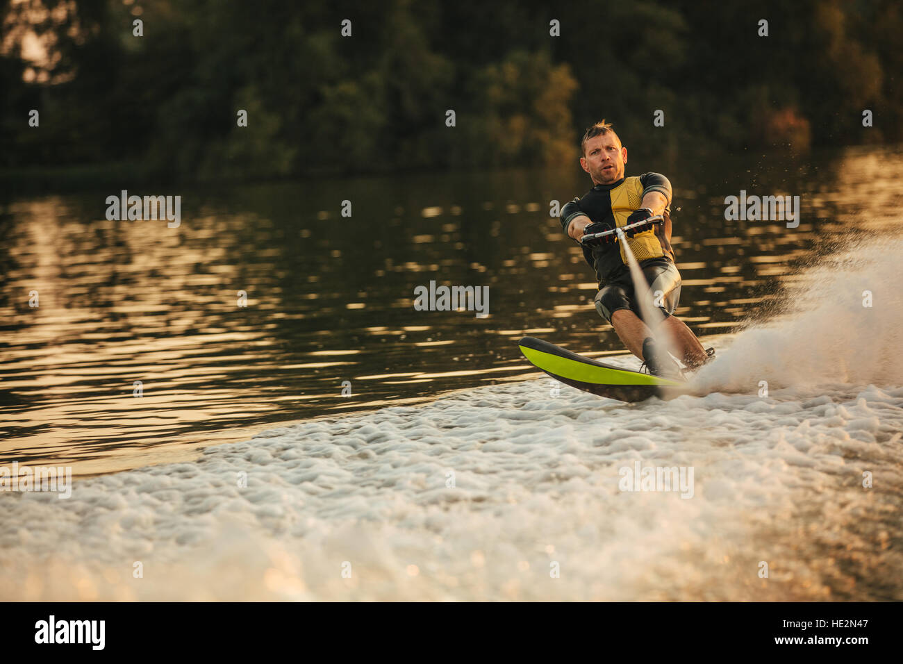 Mann reitet Wakeboard auf Welle der Motorboot in einem See. Männliche Wasserski hinter einem Boot. Stockfoto