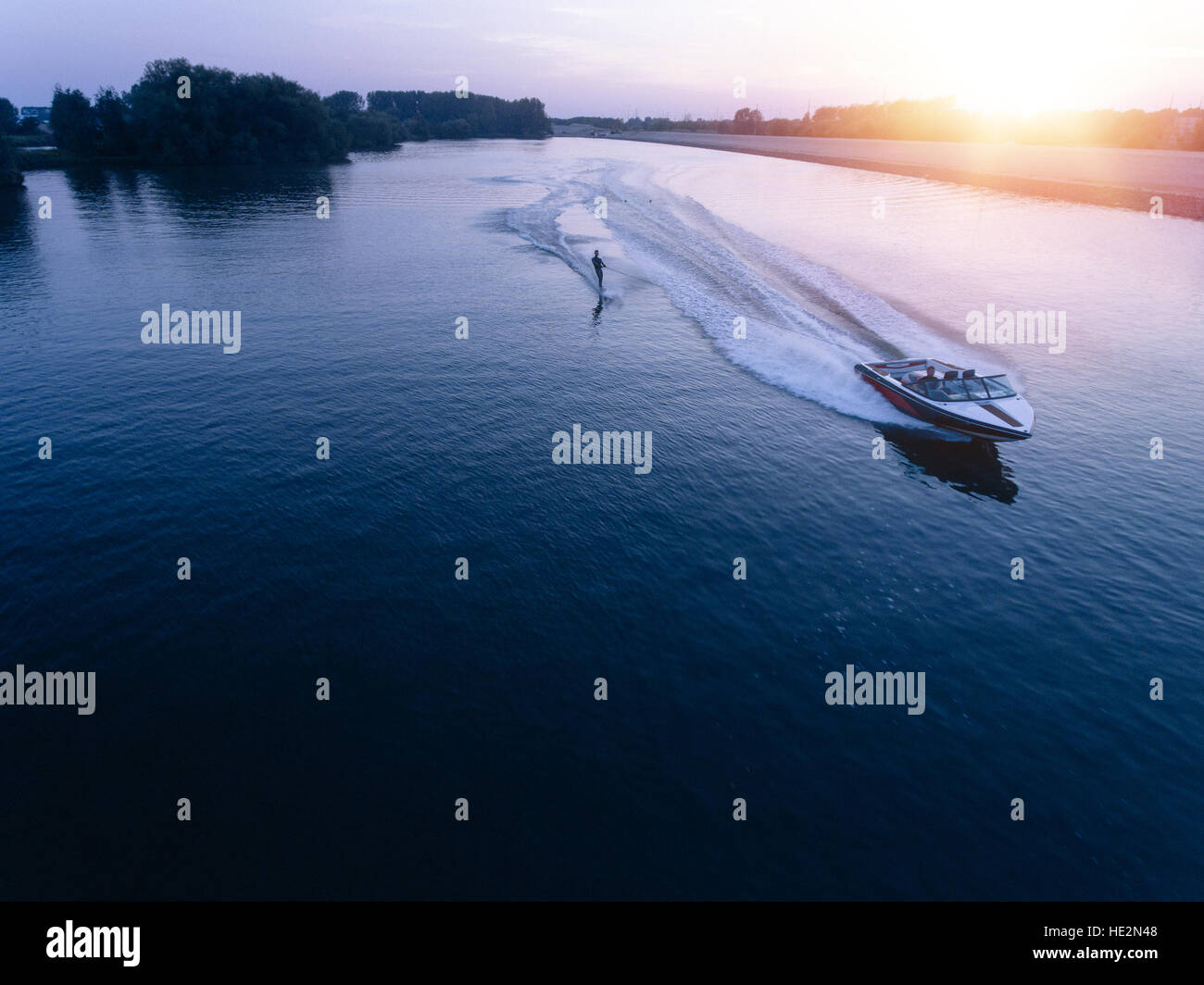 Luftaufnahme des Mannes Wakeboarden auf See bei Sonnenuntergang. Wasserski auf See hinter einem Boot. Stockfoto