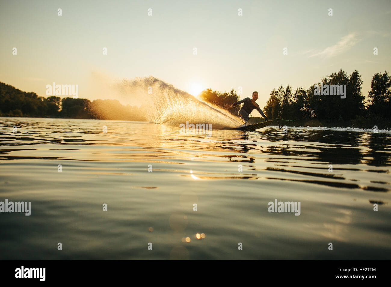 Wakeboarder bewegt sich schnell in Spritzwasser bei Sonnenuntergang. Man Wasserski an einem See. Stockfoto