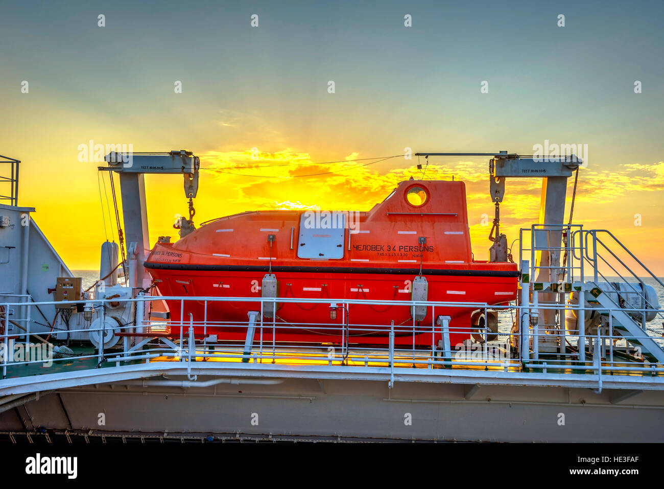 Orange Rettungsboot auf den Frachter am Meer bei Sonnenuntergang Stockfoto