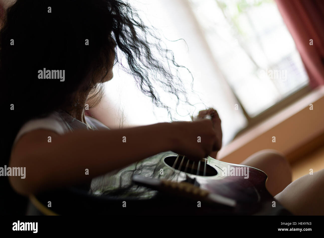Mädchen mit lockigen Haaren spielt Gitarre, eine Silhouette und Hintergrund Unschärfe, Gegenlicht Stockfoto