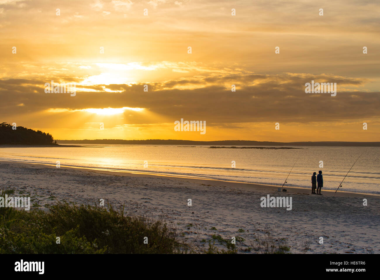 Zwei Männer stehen, Fischen und einem hellen orange und gelb Sonnenaufgang über Callala Bucht an der Südküste von New South Wales in Australien Stockfoto