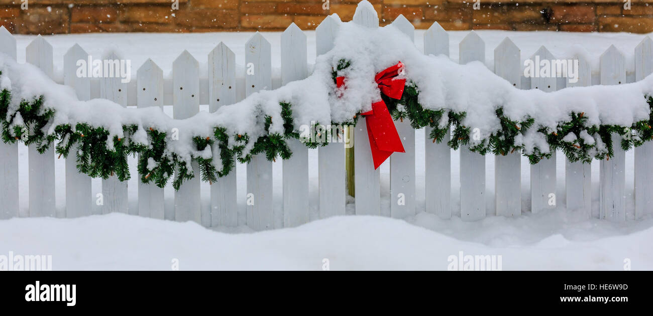 Weißer Lattenzaun für Weihnachten dekoriert mit roter Schleife und Grünen Kranz im Schnee. Stockfoto