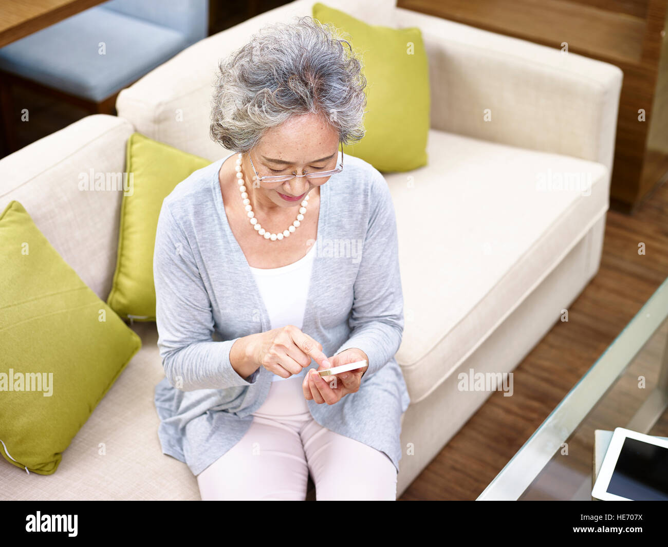 erhöhte Ansicht einer senior asiatische Frau sitzt auf dem Sofa mit Handy. Stockfoto