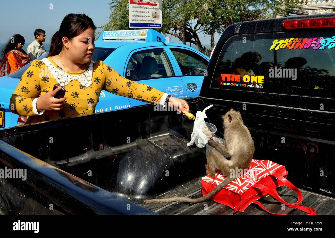 Bang Saen, Thailand: Thai-Frau bietet eine Banane mit einem Affen sitzen oben auf eine Umhängetasche im hinteren Teil ein Pickup-truck Stockfoto