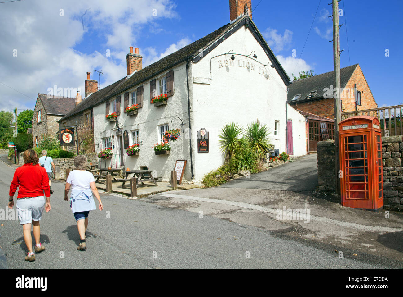 Menschen zu Fuß vorbei an der Red Lion Pub und rote Telefonzelle am Hognaston in der Nähe von Ashbourne Derbyshire England Stockfoto