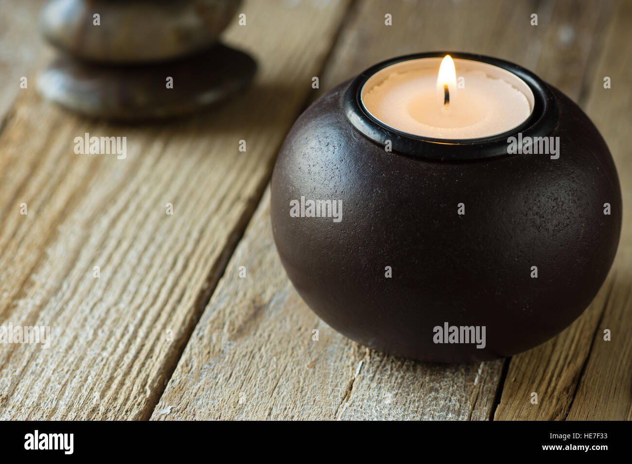 Weißer Tee Licht in einem schwarzen Holz Kerzenständer und Zen ausgewogen Steinen im Hintergrund, Exemplar für Text, Konzept der Harmonie, Frieden Stockfoto