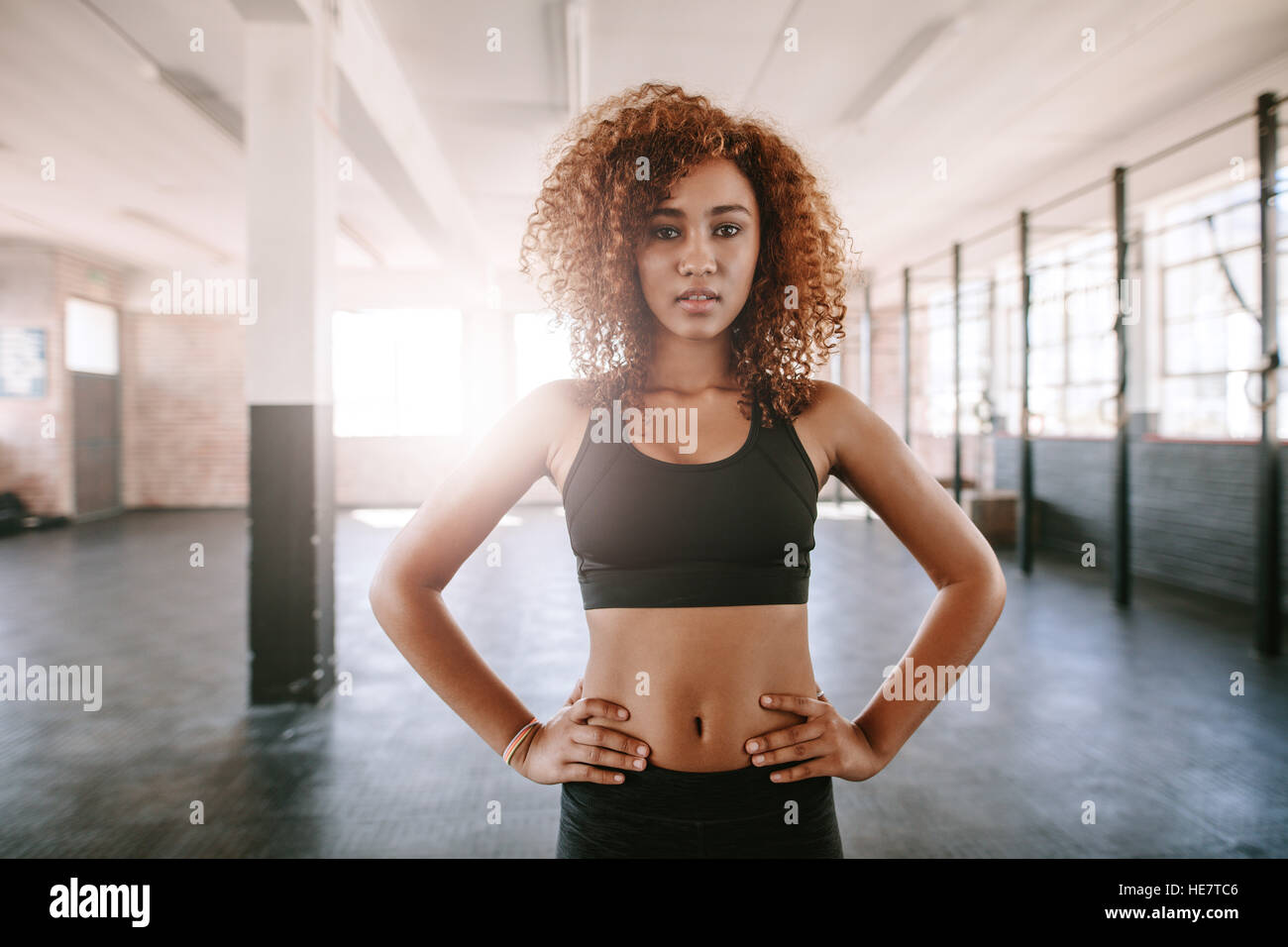 Porträt einer fitten jungen afrikanerin, die mit Händen auf Hüften im Fitnessstudio steht. Fitnessmodell posiert vor der Kamera. Stockfoto