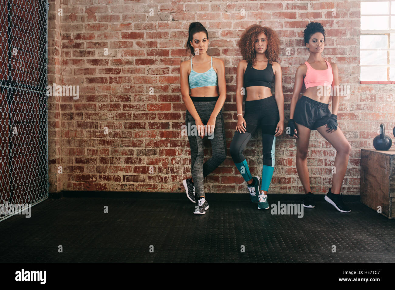 Voller Länge Schuss drei junge Frau in Sportkleidung stehen gemeinsam in der Turnhalle. Gemischtrassig Frauen im Fitnessraum Blick in die Kamera. Stockfoto