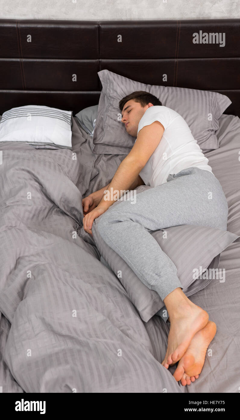 Schön müde Mann im Pyjama schlafen alleine ohne Decke in stilvolles Bett in  grauen Farben und in der Nähe von Nachttisch mit Kerzen in einem  Schlafzimmer im Dachboden st Stockfotografie - Alamy