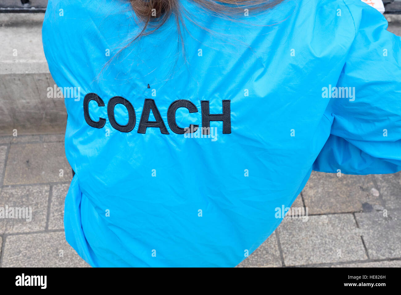 Eine junge Frau trägt eine helle blaue Jacke mit Coach bestickt auf der Rückseite Stockfoto