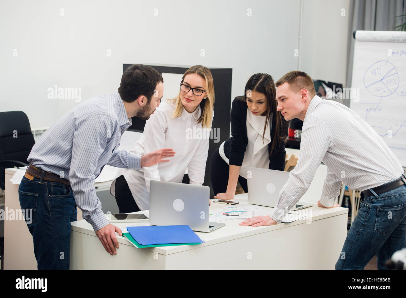 Willkommen Sie an Bord. Vier am Tisch während zwei von ihnen Geschäftsleute Händeschütteln und lächelnd Stockfoto