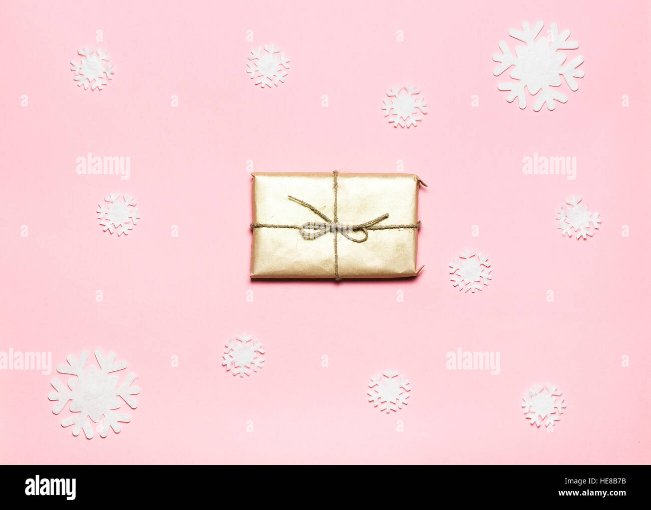 Nahaufnahme des kleinen Geschenk verpackt mit Band auf rosa Hintergrund dekoriert Schneeflocken... Weihnachten. Minimal-Konzept. Flach zu legen. Ansicht von oben. Stockfoto