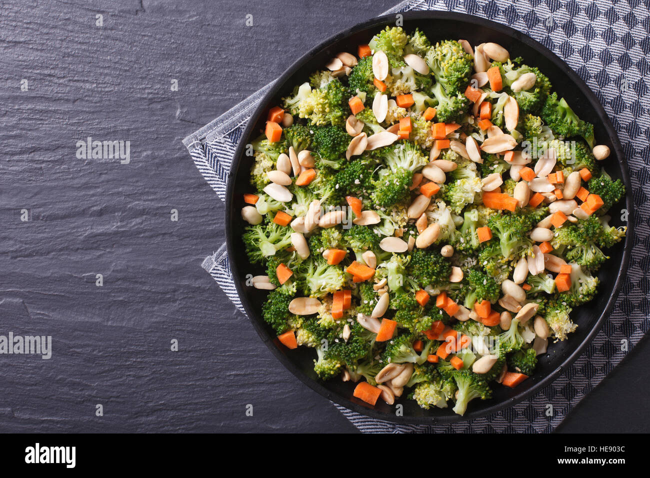 Gesunde Ernährung: Broccoli-Salat mit Erdnüssen und Karotten Nahaufnahme auf einer schwarzen Platte. horizontale Ansicht von oben Stockfoto