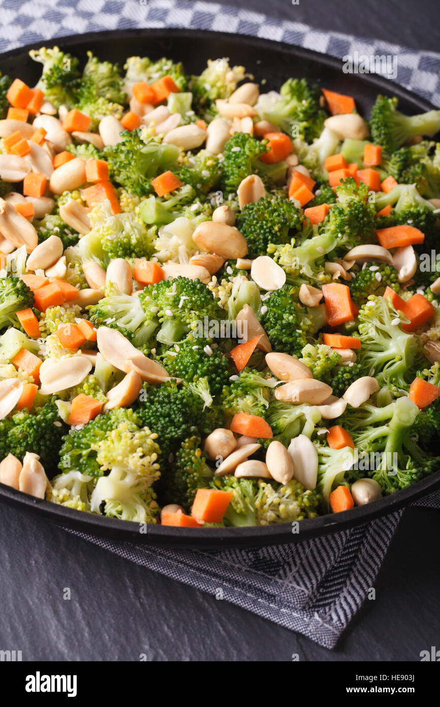 Brokkoli mit Erdnüssen und Karotten Nahaufnahme auf einer schwarzen Platte. vertikale Stockfoto