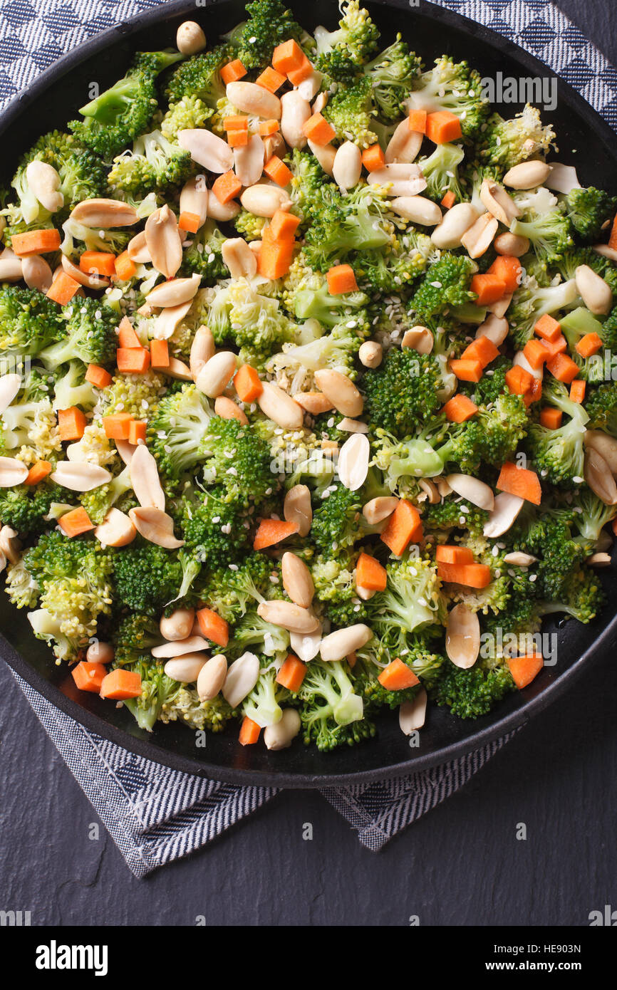 Brokkoli mit Erdnüssen und Karotten Nahaufnahme auf einer schwarzen Platte. Vertikale Ansicht von oben Stockfoto