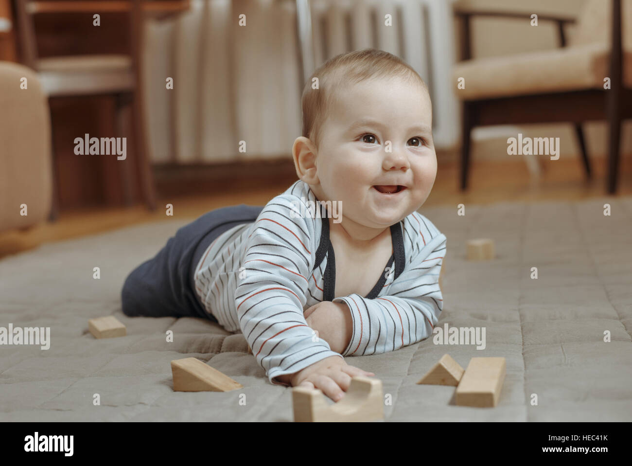 Niedliche glücklichen kleinen Jungen spielen auf dem Teppich zu Hause liegen auf dem Bauch nach oben auf die Seite mit einem strahlenden Lächeln Stockfoto