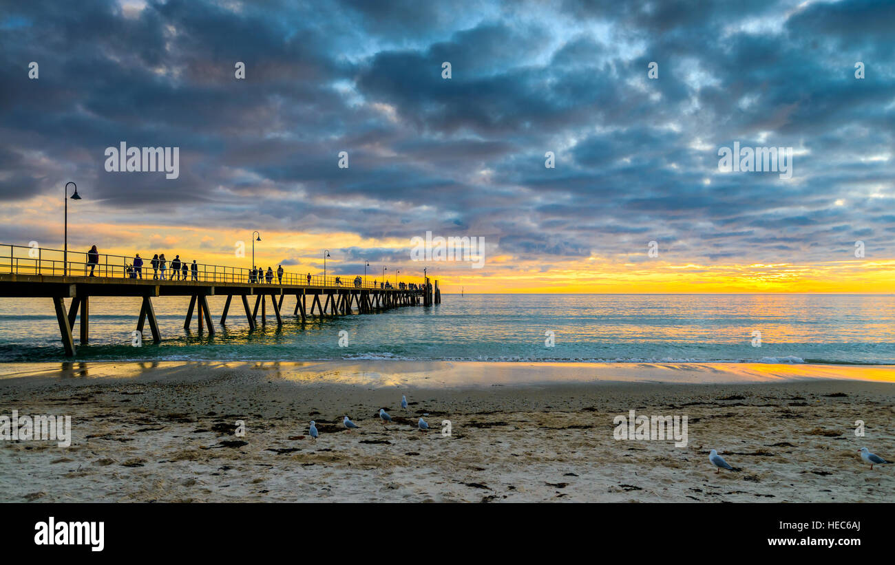 Menschen zu Fuß entlang Glenelg Beach Pier bei Sonnenuntergang, South Australia Stockfoto