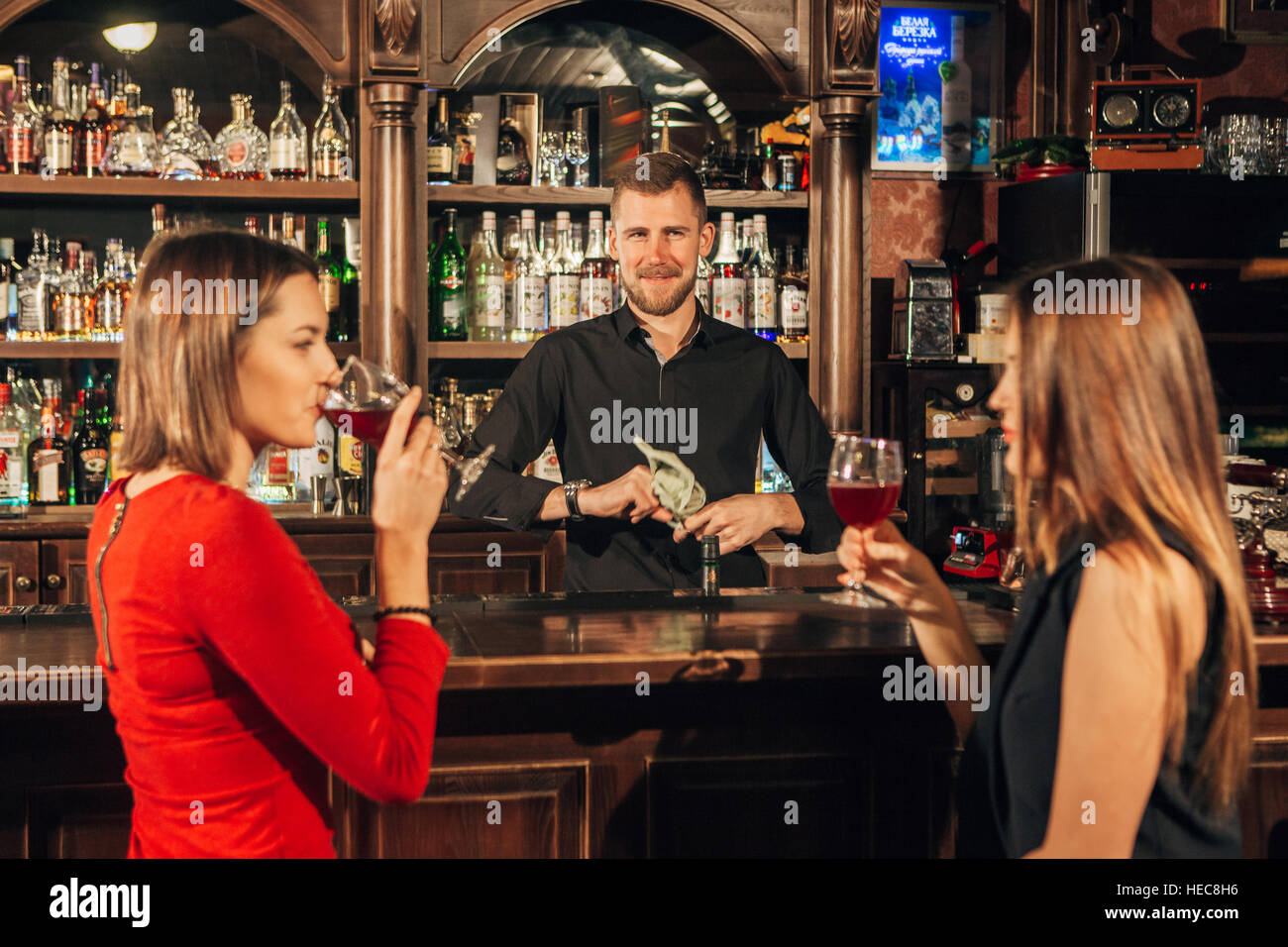 Zwei attraktive junge Frauen treffen sich in einer Kneipe für Glas Rotwein sitzen an Theke Lächeln einander Stockfoto