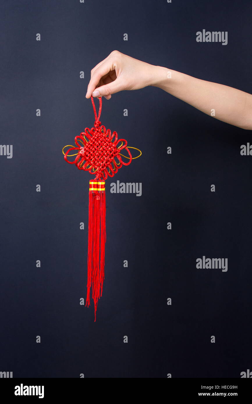 Weibliche Hand Holding chinesischen roten Knoten auf dunklem Hintergrund Stockfoto