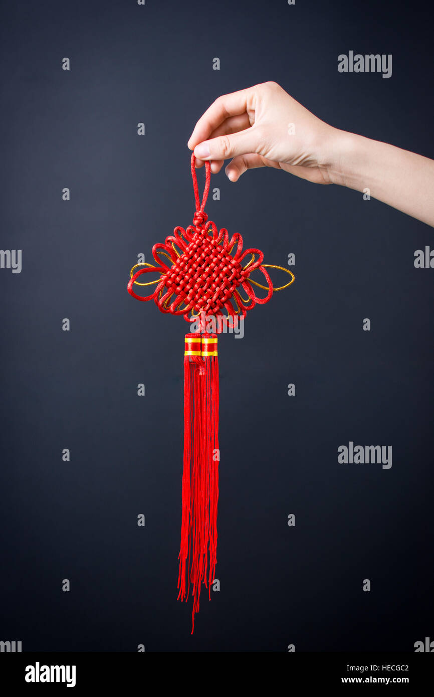 Weibliche Hand Holding chinesischen roten Knoten auf dunklem Hintergrund Stockfoto