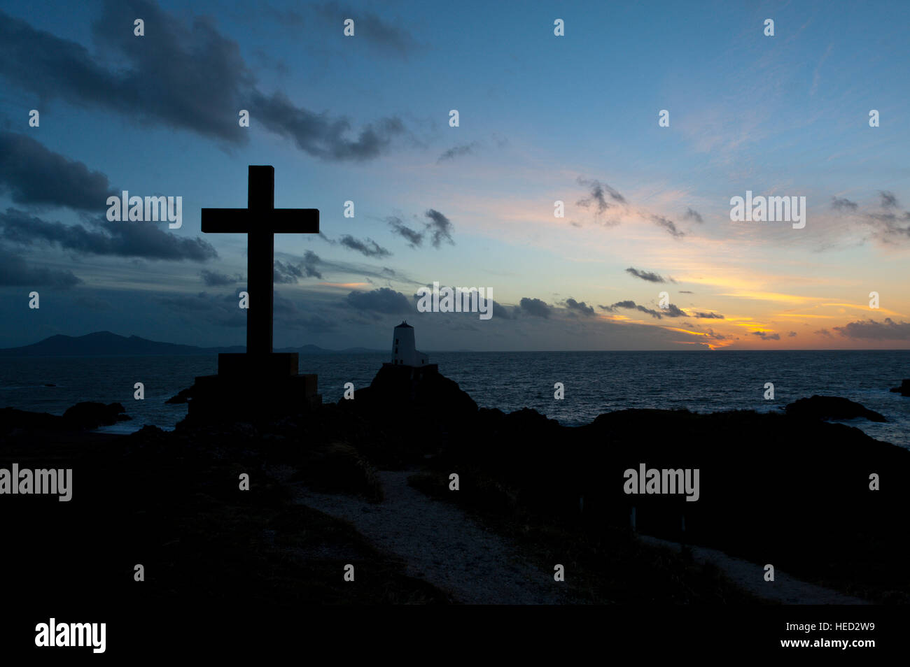 Newborough, Isle of Anglesey, Wales, UK. 21. Dezember 2016. Das Wetter.  St Dwynwens Cross und dem alten Leuchtturm sind am Abend der Wintersonnenwende der kürzeste Tag des Jahres 2016 gegen die untergehende Sonne auf Llanddwyn Island, aka Ynys Llanddwyn Silhouette. Das Wetter.  (Tageslicht) Daylength heute in London, UK werden 7 Stunden 49 Minuten 40 Sekunden. © Graham M. Lawrence/Alamy-Live-Nachrichten. Stockfoto