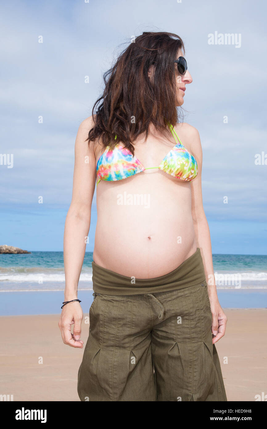 Brünette braune Haare schwangere Frau mit Bikini Top grüne Hose und  schwarze Sonnenbrillen suchen beiseite im Sommer im Urlaub Strand in  Asturien Spanien Stockfotografie - Alamy