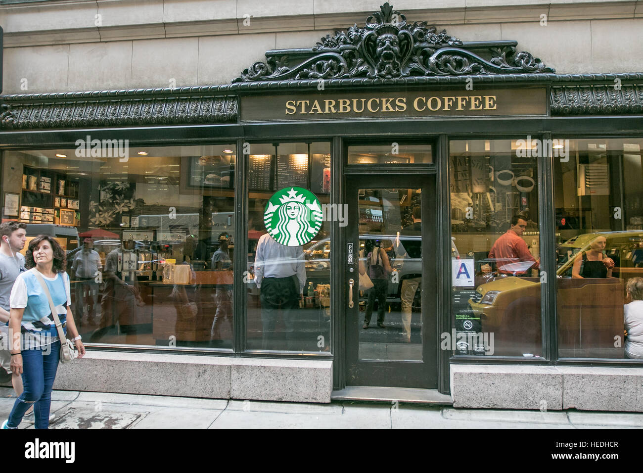 Eine Ladenzeile für einen Starbucks Coffee Shop-Standort in Manhattan mit Menschen zu Fuß durch und drinnen sitzen. Stockfoto