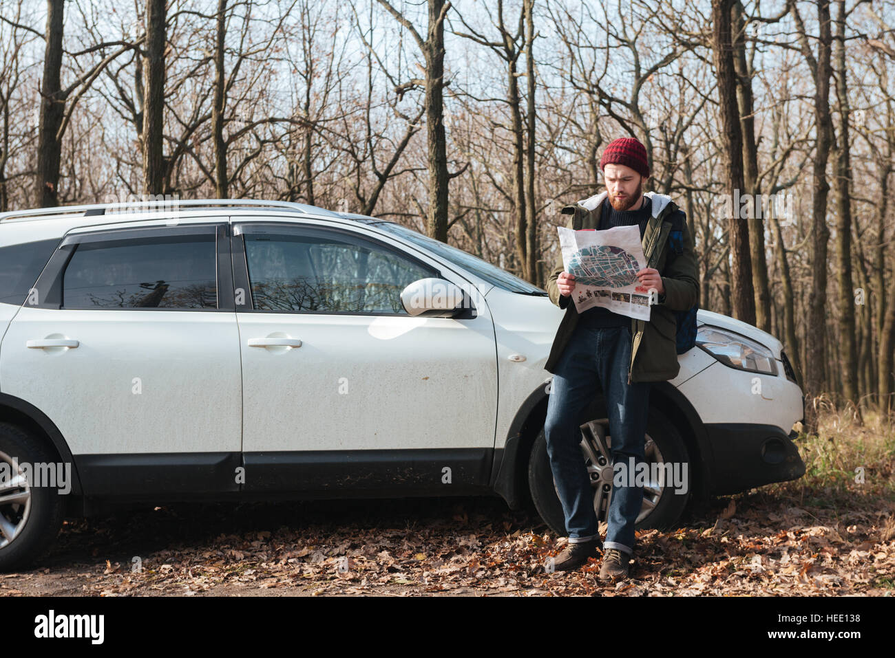 Verwirrt bärtiger Mann mit Hut Blick auf Karte im Wald stehen in der Nähe von Auto Bild. Stockfoto