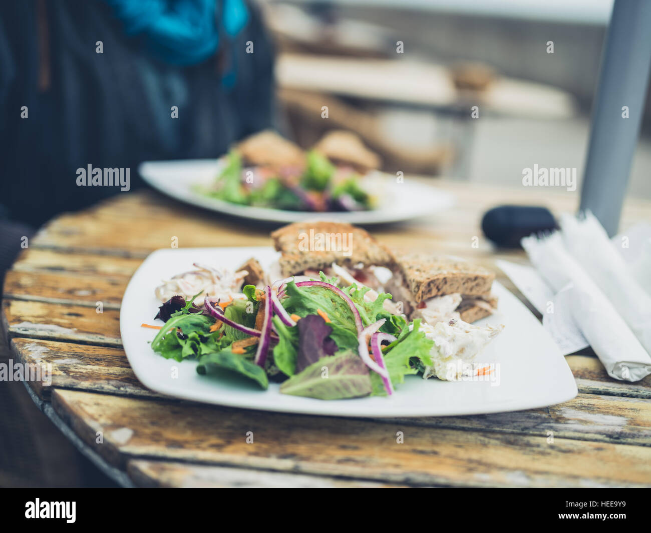 Ein Teller mit Salat und Hähnchen-Sandwich auf einen Tisch draußen mit einer Frau im Hintergrund Stockfoto