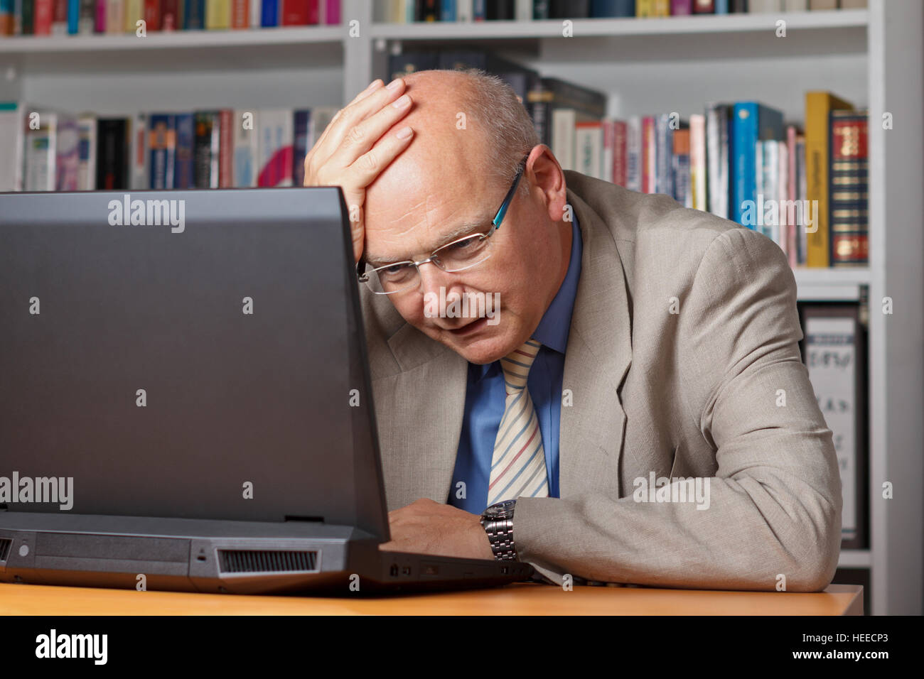 Älterer Mann in Jackett und Krawatte in seinem Büro betäubt und vor seinem Notebook betonte, schlechtes Geschäft, Krise, Frustration Stockfoto
