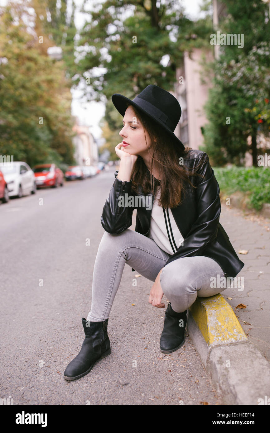 Junge Frau sitzt auf der Straße, mit Hut und Leder Jacke Stockfoto