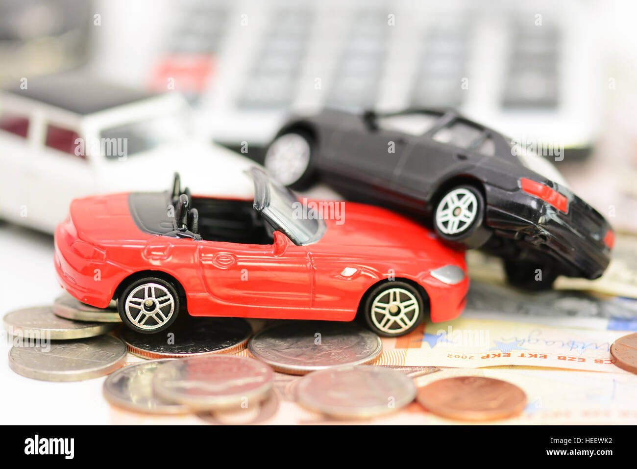 Auto-Versicherung-Konzept mit bunten Spielzeug-Autos, Autoschlüssel, Münzen und Scheine Stockfoto