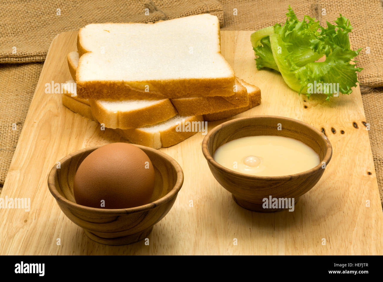 Haufen von geschnittenem Brot, gezuckerte Kondensmilch und Ei auf einem Holzbrett Stockfoto