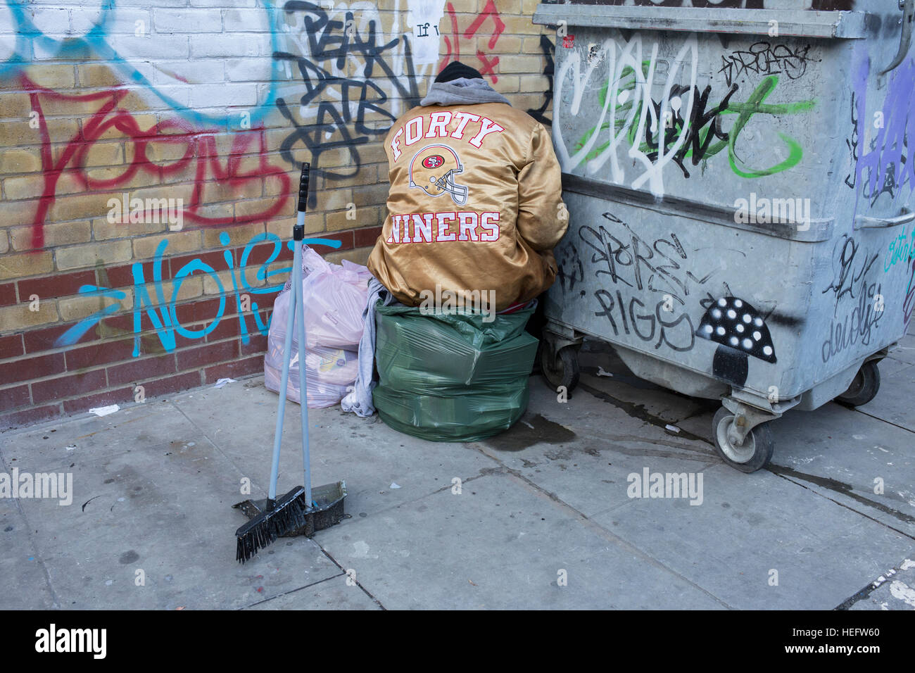 Aufgenommen in East London, UK. Ein Mann mit einer San Francisco 49ers Jacke deckt seine Tätigkeit von Passanten. Stockfoto