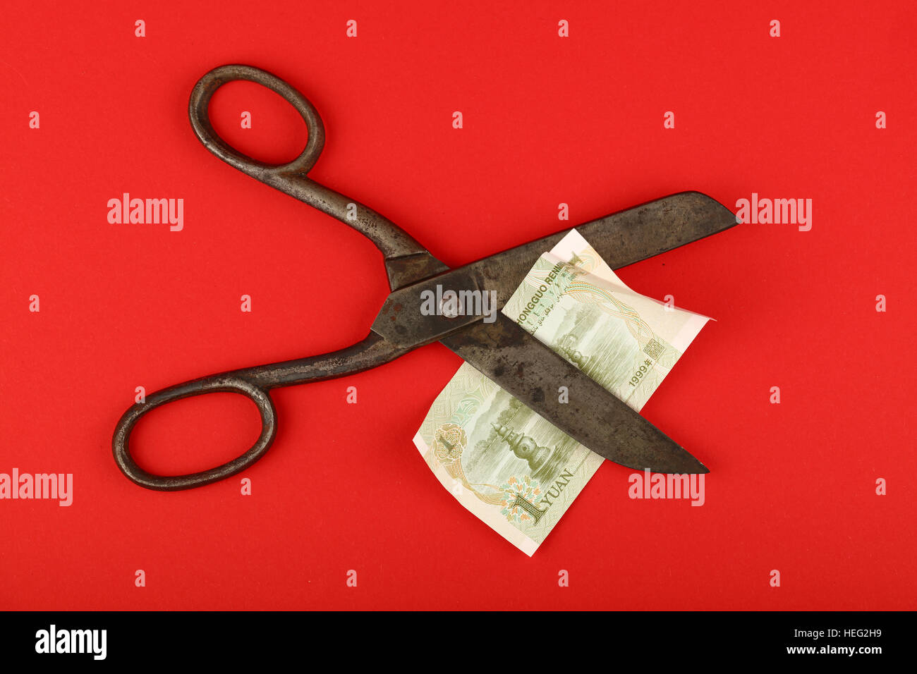 China Finanzkrise, Rückgang der chinesischen Wirtschaft und Yuan Wechselkurs illustrierte, alte Vintage Schere schneiden einer Yuan-Banknote auf rotem Grund Stockfoto