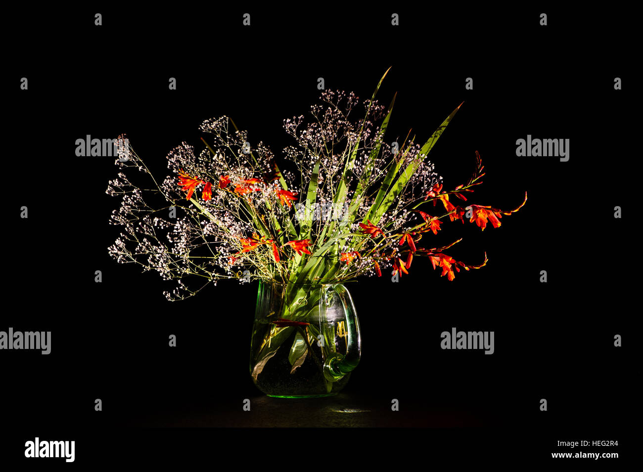 Ein Bouquet mit Montbretia und Schleierkraut Paniculata in ein grünes Glas kann auf einem schwarzen Hintergrund Stockfoto