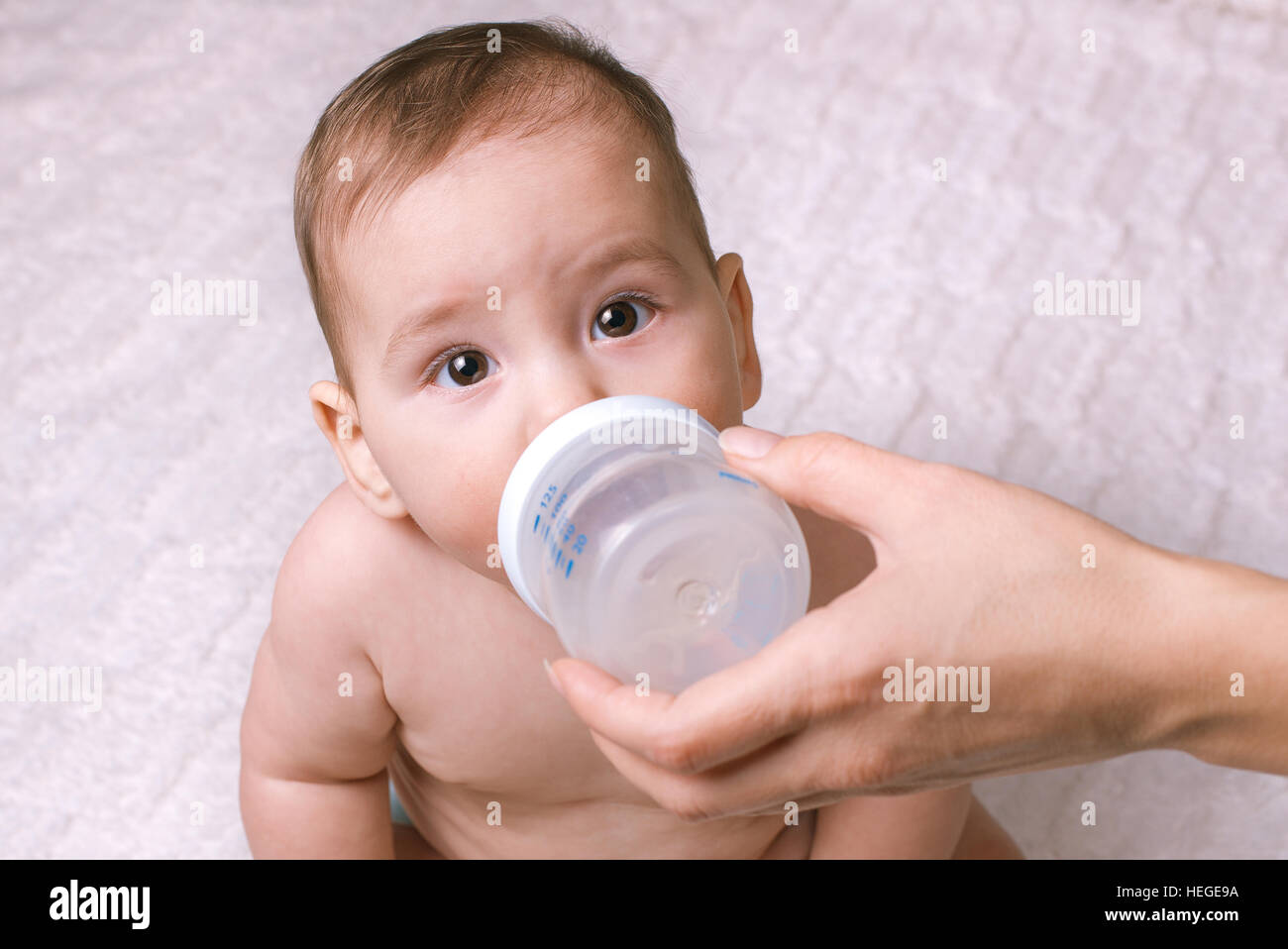 Süße kleine Baby gefüttert aus einer Flasche über die Spitze in die Kamera starrte mit weit aufgerissenen Augen Neugier Stockfoto