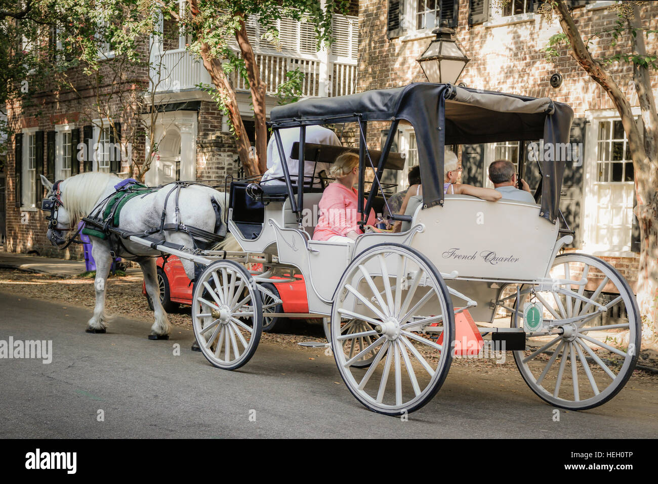 Ein schönes weißes Pferd zieht einen Vintage Wagen zusammen mit einem Reiseleiter und Touristen rund um die historische Innenstadt von Charleston, SC Stockfoto