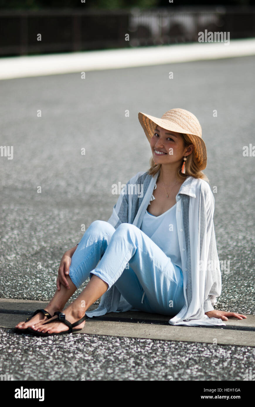 Glückliche, schöne Japanerin ist trägt einen Strohhut und lächelt in die Kamera auf dem Boden sitzen. Stockfoto